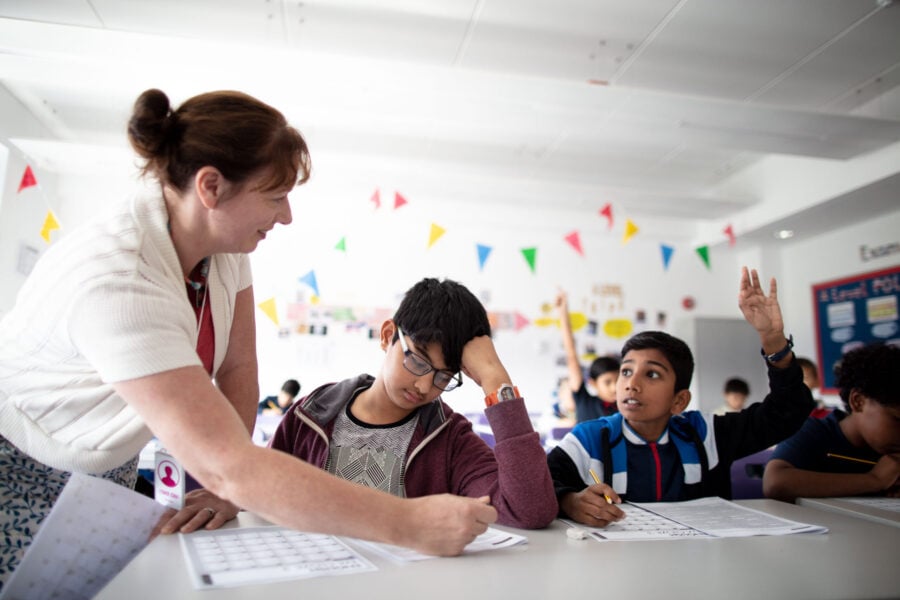 A teacher leaning over a desk of smiling pupils in a Test Teach class